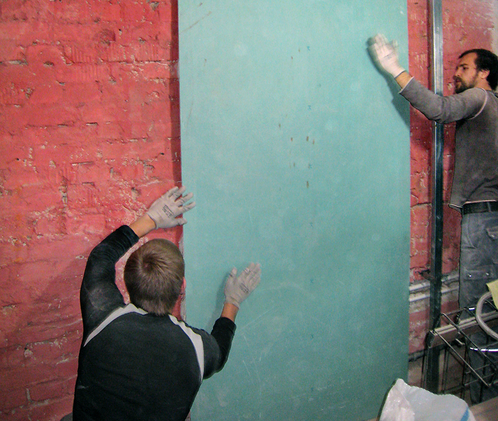 Мастера крепят гипсокартон к кирпичной стене