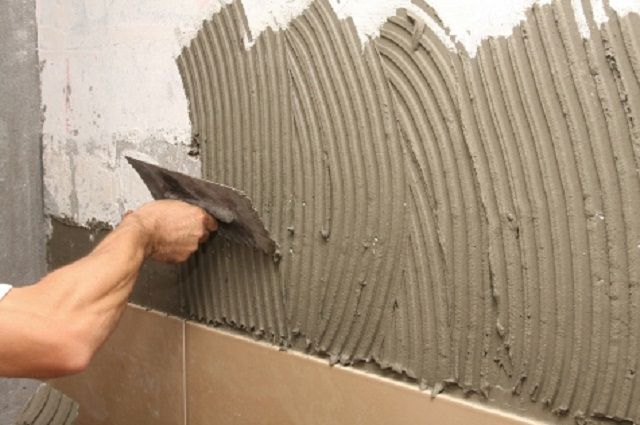 Нанесение и распределение клея на поверхности стены печки